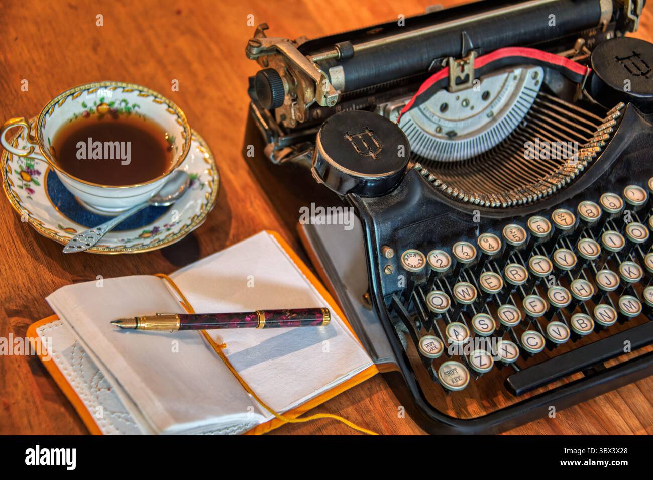 typewriter mechanical siting on a wooden table in the room, tea cup porcelain on the desk, paper notebook with fountainpen, home office Stock Photo