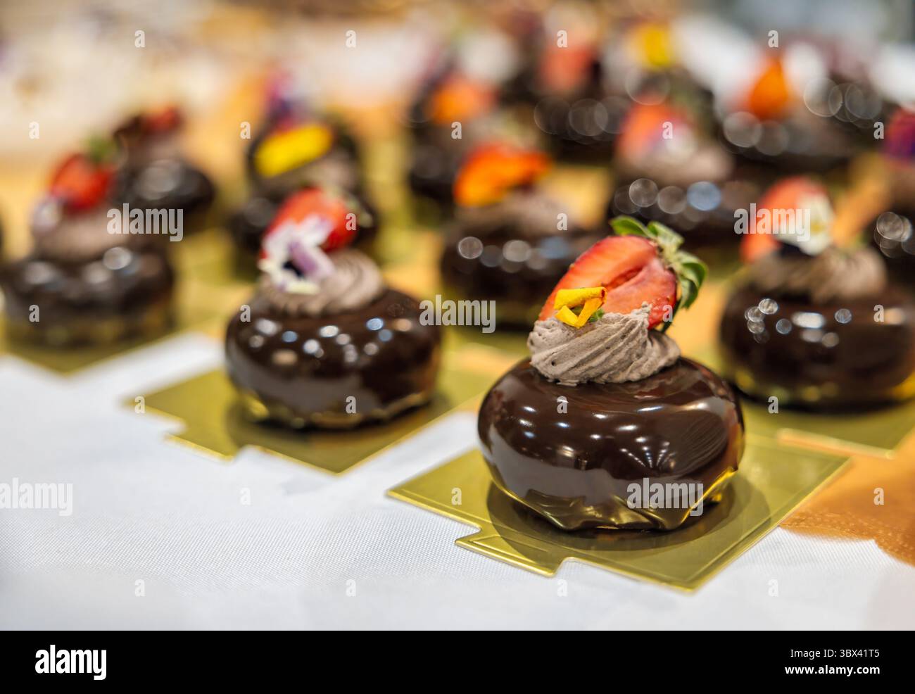 Dark chocolate mousse mini cakes with strawberry and edible flowers, decadent patisserie mousse on display on golden plates Stock Photo