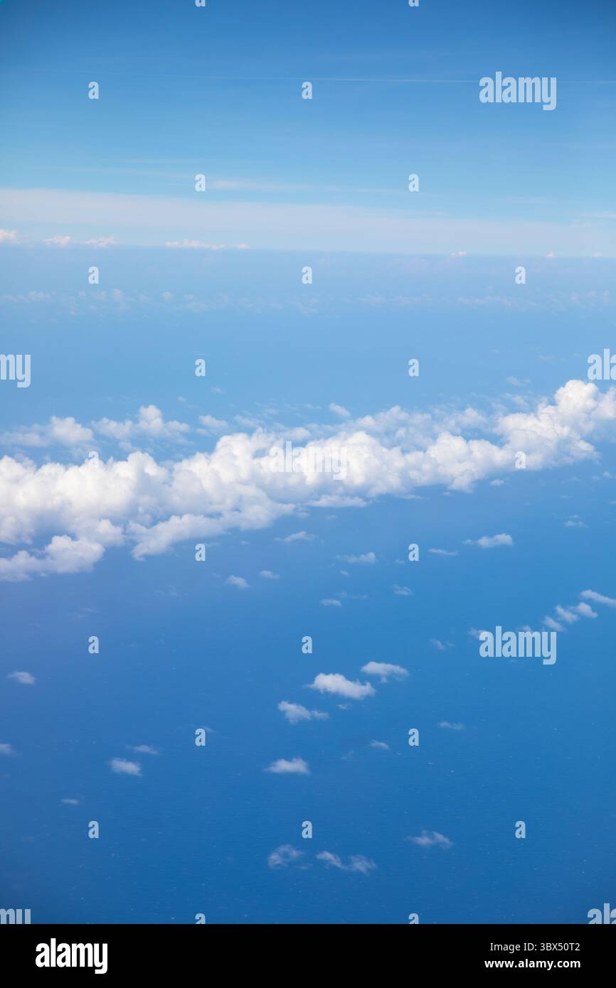 Fluffy white clouds drift across a vibrant blue sky above a vast ocean ...