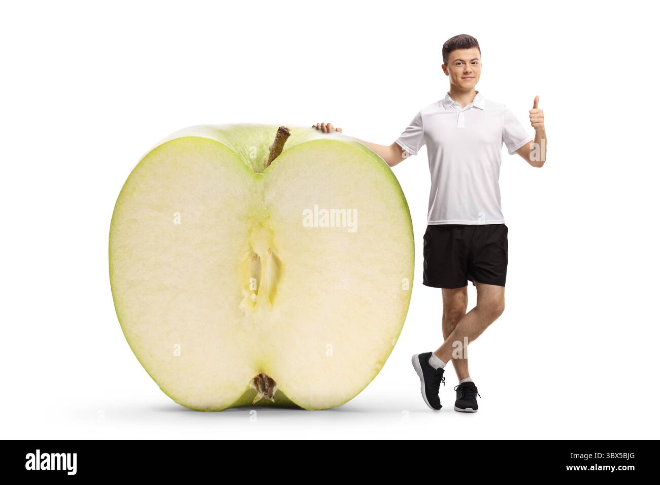 Full length portrait of a young man in sportswear leaning on a big apple and gesturing thumbs up isolated on white background Stock Photo
