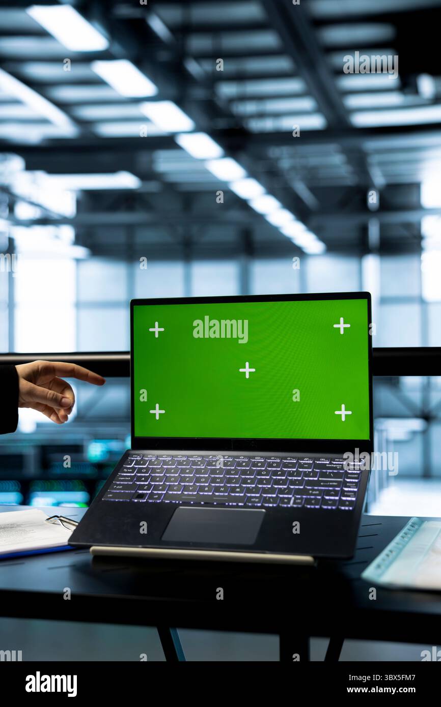 Technicians in data center using green screen mockup laptop, inspecting server clusters, updating network topologies. IT experts using chroma key notebook, ensuring stable operations Stock Photo