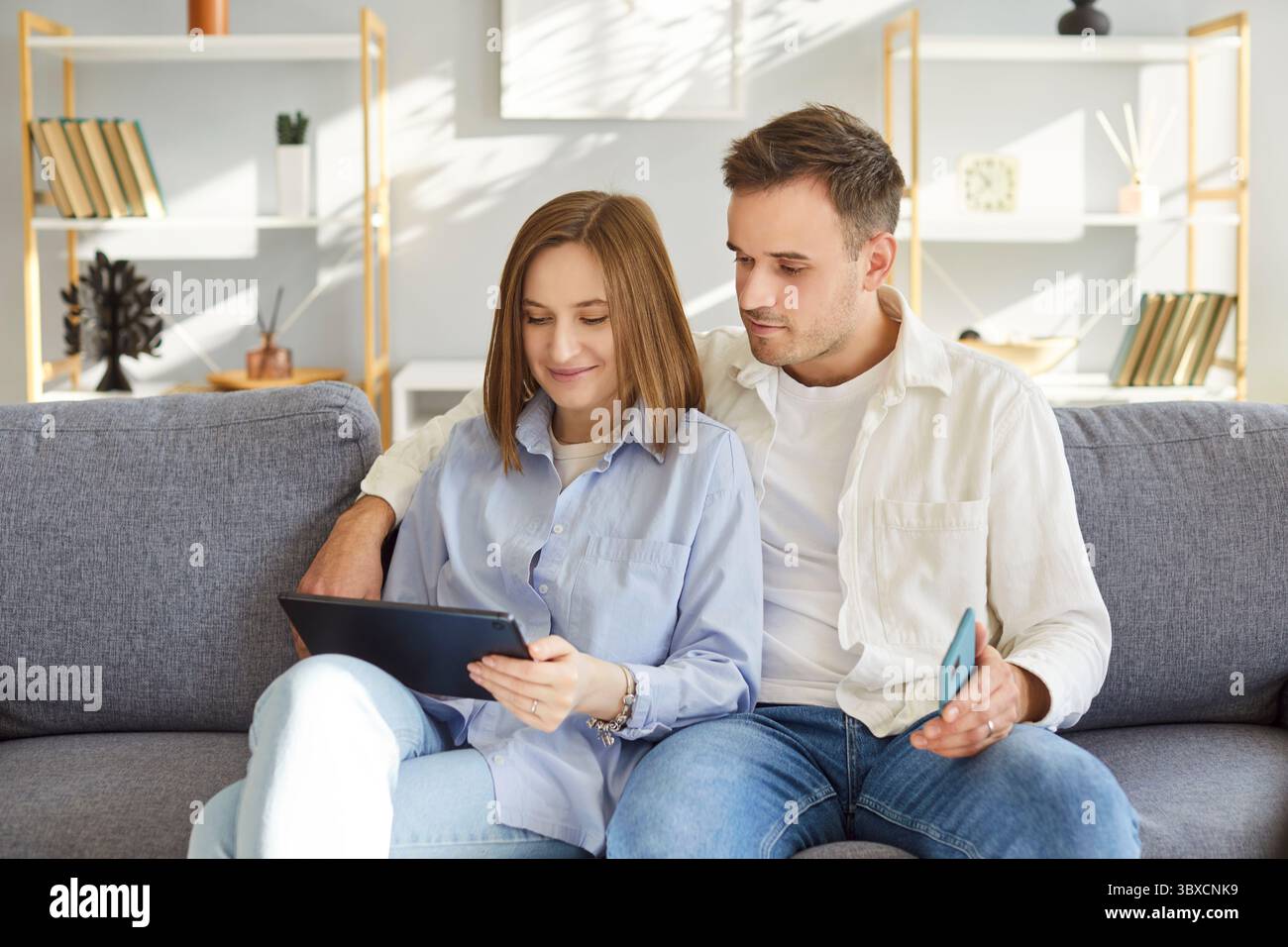 Happy spouses, smiling couple in love using tablet computer together at home, talking on video call Stock Photo