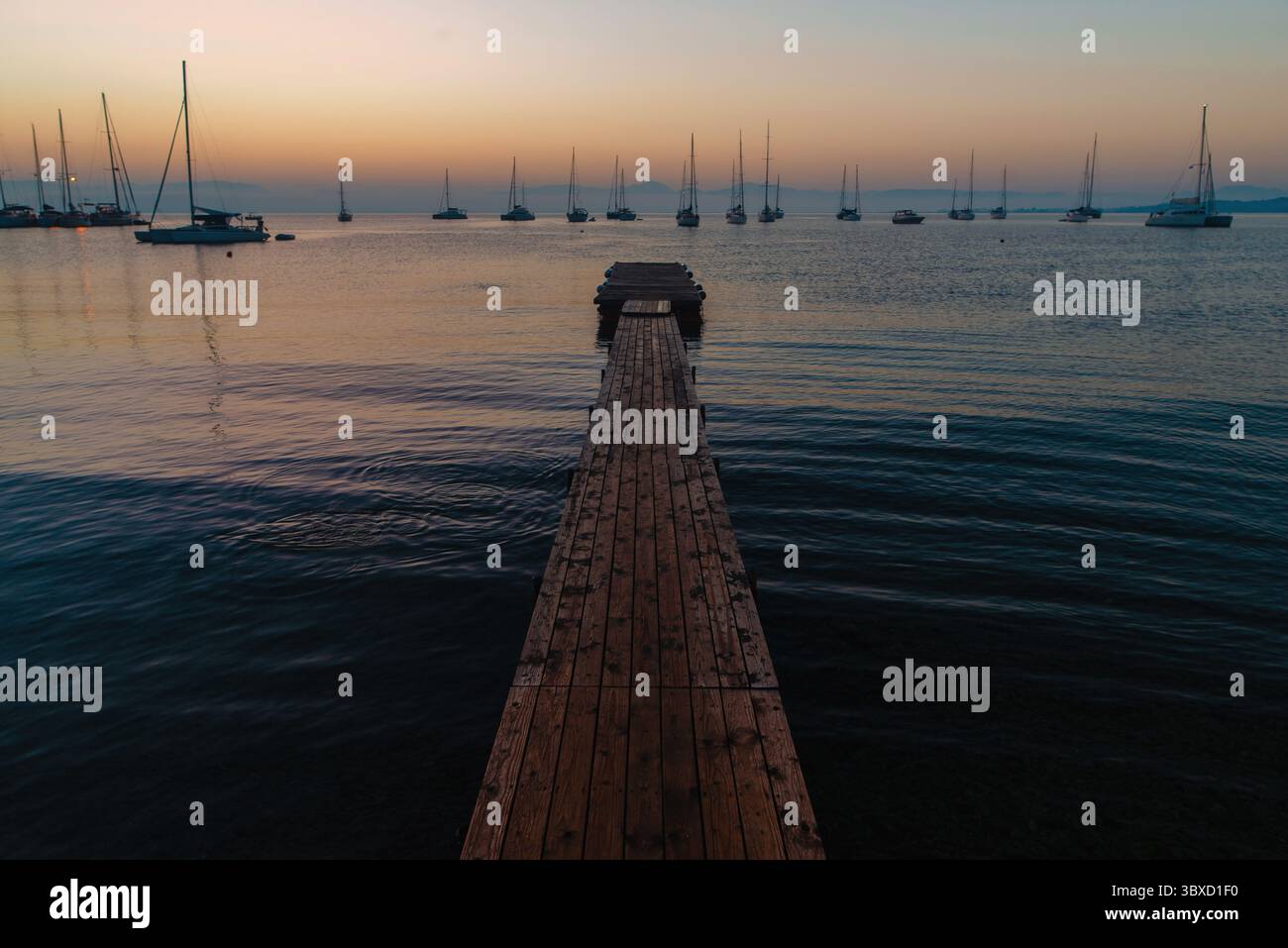 Serene Sunset Over Pier and Sailboats Stock Photo