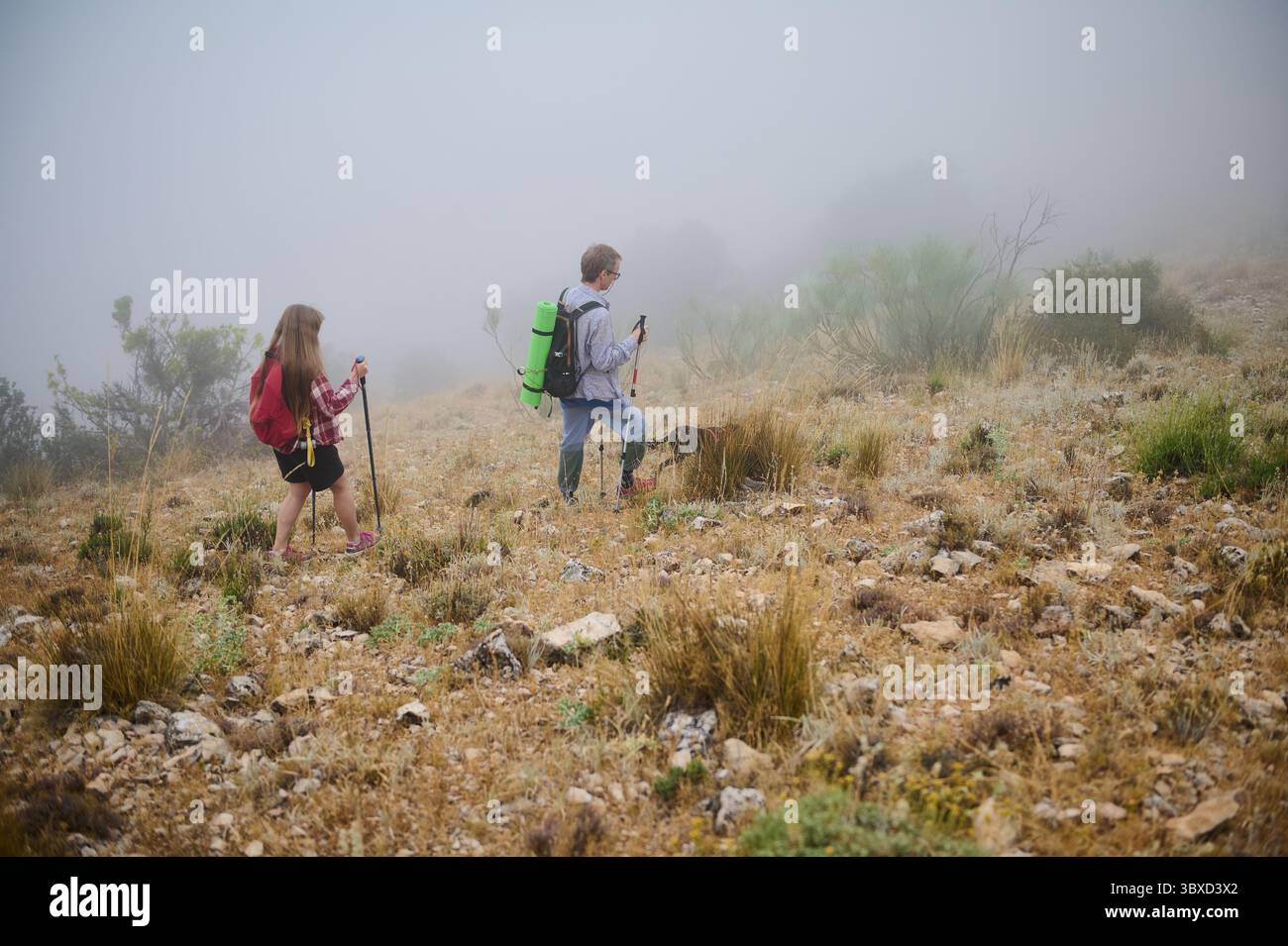 Two hikers with backpacks navigate through a foggy mountain terrain ...