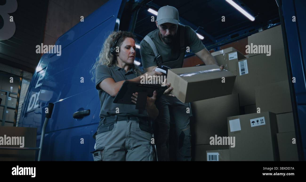 Outside of Logistics Warehouse at Night: Female Inventory Specialist Using Tablet Computer, Male Loader Checking Cardboard Boxes with Online Orders, Goods in Delivery Truck for Shipping to Customers. Stock Photo