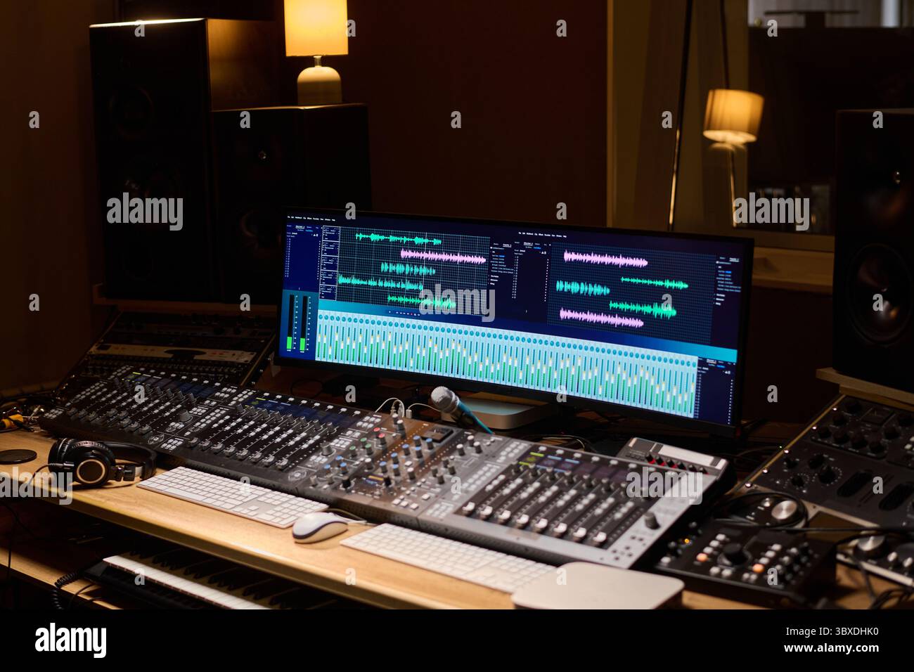 Professional audio mixing console with large monitor displaying digital audio workstation interface showing multiple tracks, headphones resting on desk, studio speakers in background Stock Photo