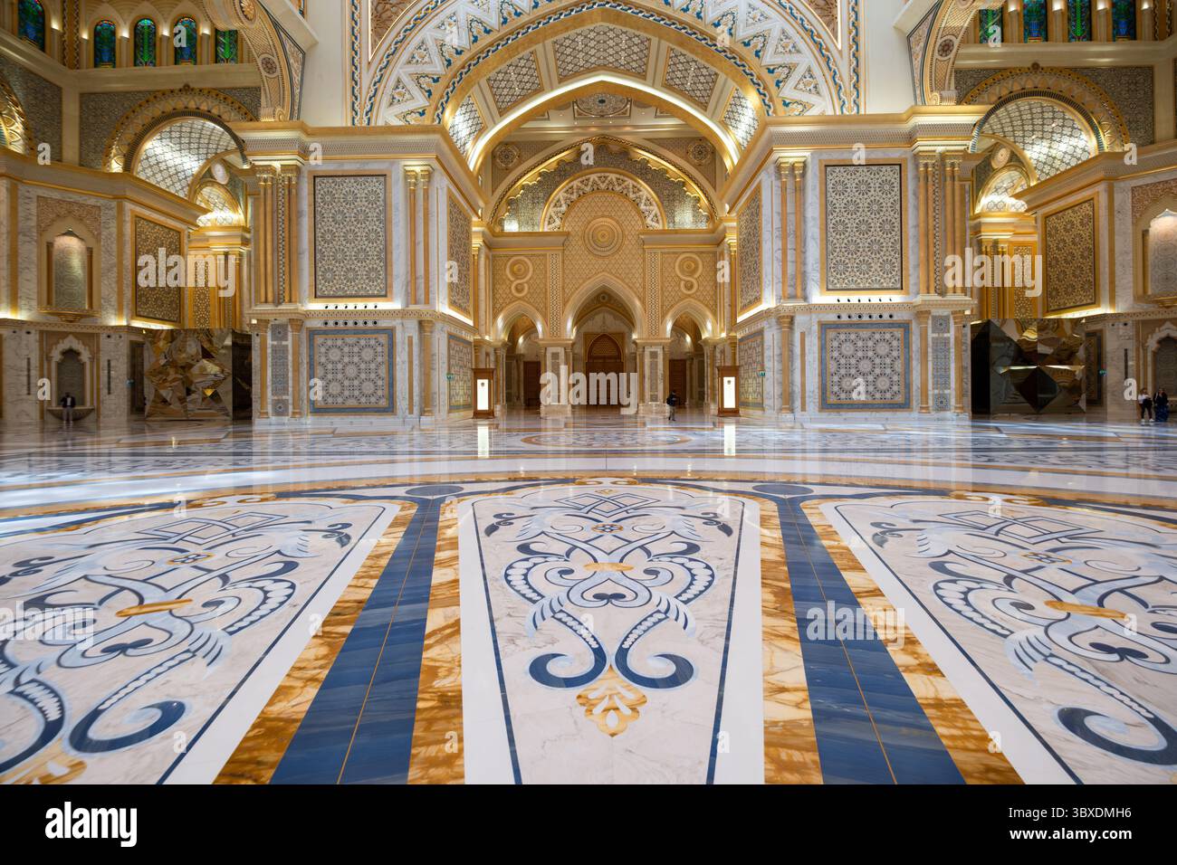 Expansive, ornate palace hall with exquisite patterns on walls and floor, featuring intricate ceilings and grand arches; minimal people in view, dress Stock Photo