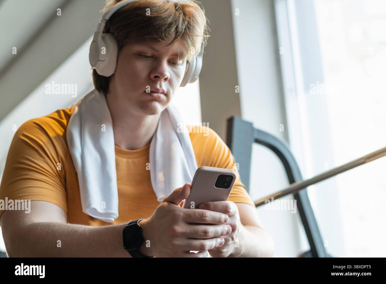Sporty young man relax and sitting with mobile phone, listen music headphones and texting at gym. Bodybuilder during training . Fitness lifestyle conc Stock Photo