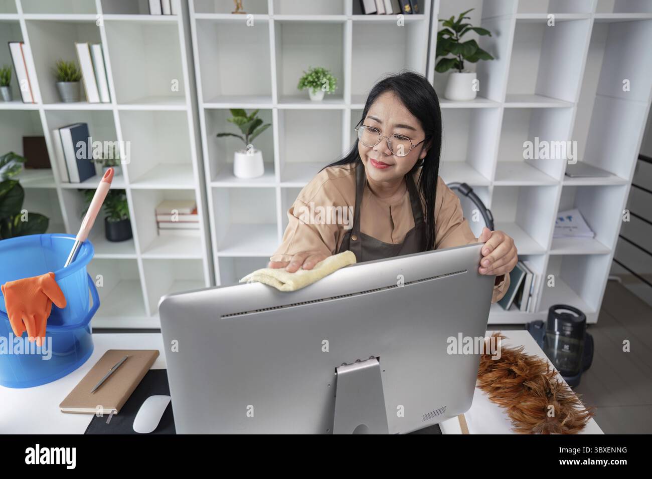 A dedicated housekeeper meticulously cleaning an office desk with a cloth, ensuring a spotless and organized workspace Stock Photo