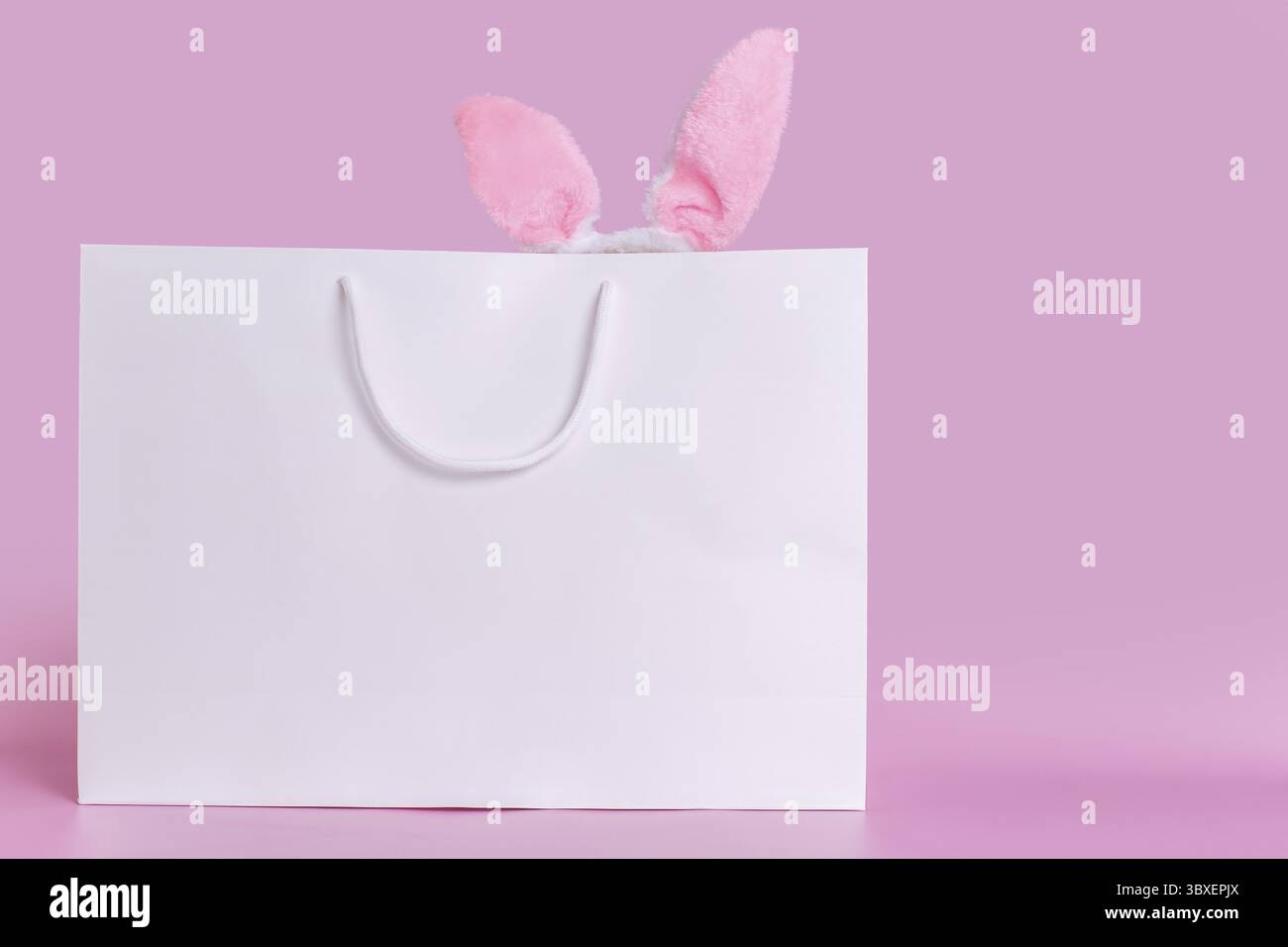 A big white paper bag on a pink background with pink fluffy ears, standing on a pink background. Copy space. Happy Easter concept Stock Photo