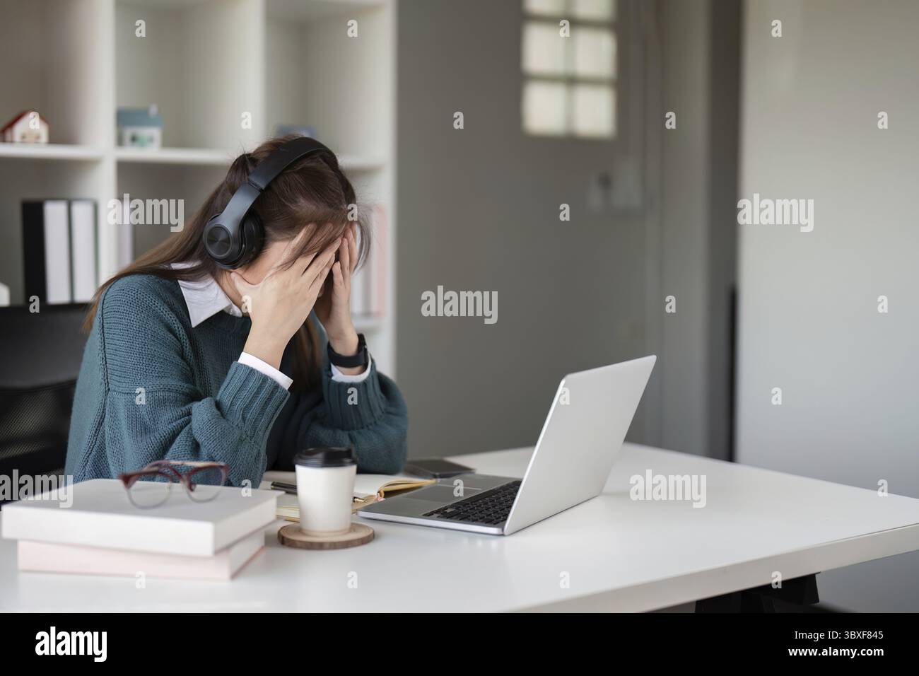 Young woman feeling stressed while wearing headphones and using a laptop in a home office Stock Photo