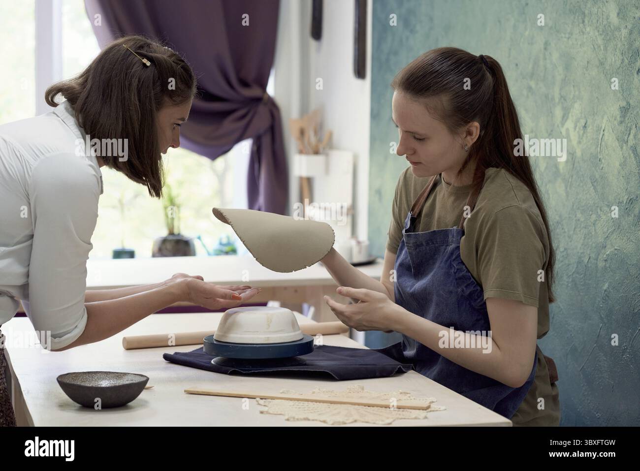 Young skillful pottery master teaching apprentice sculpting mud bowl in creative art studio Stock Photo