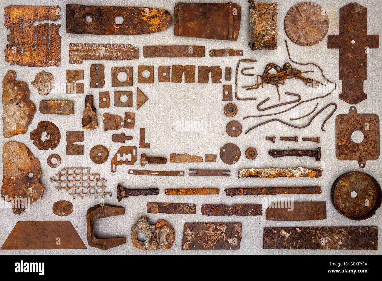 A group of various old rusty bits and pieces arranged on a concrete surface. Old rusty nuts, bolts, nails and other parts flay lay on gray background. Stock Photo