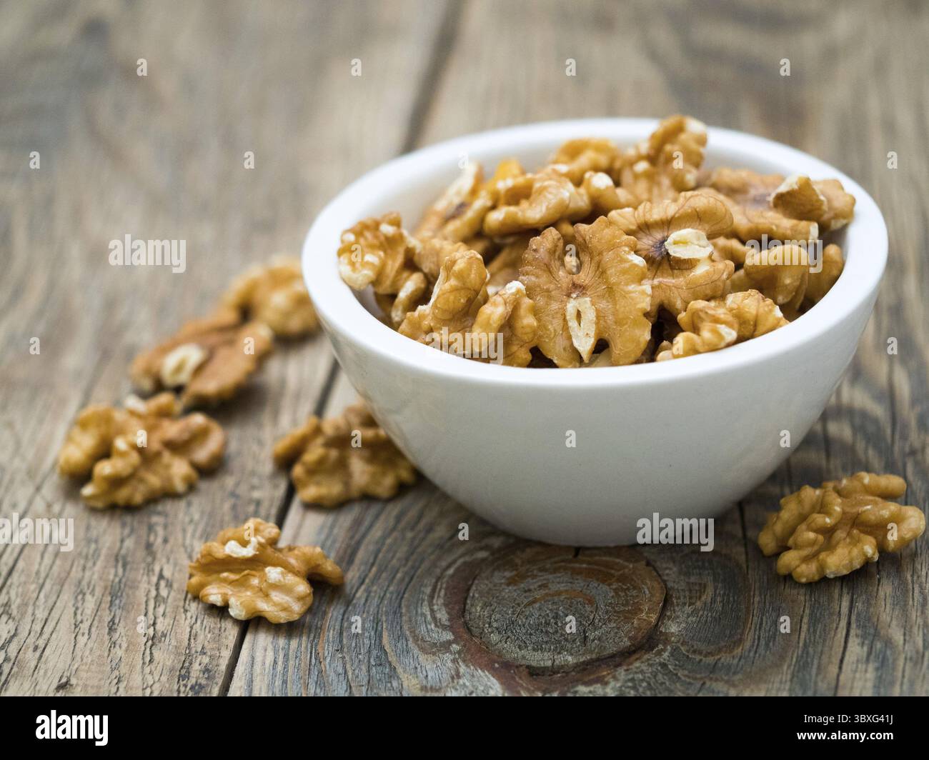 White cups with walnut, bowls with handful of nuts on grey wooden background. Selective focus, soft, side view Stock Photo