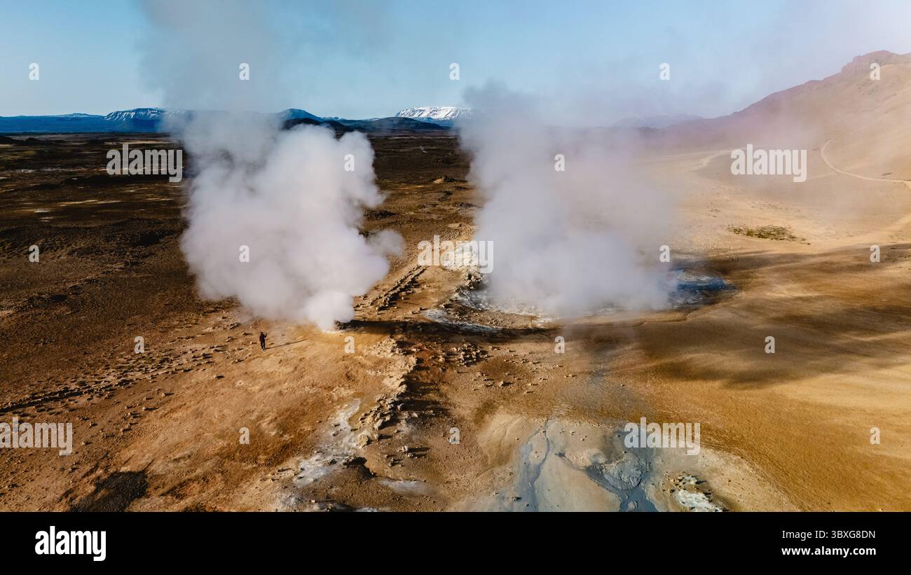 Expansive Hverir geothermal area in Iceland reveals steaming vents rising from the earth, surrounded by a unique, arid landscape. The distant mountains add to the stunning natural beauty. Stock Photo