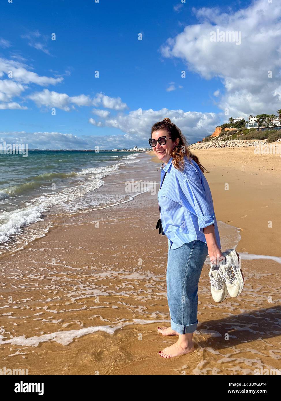 Woman in midlife walks along sandy beach, barefoot and carefree ...
