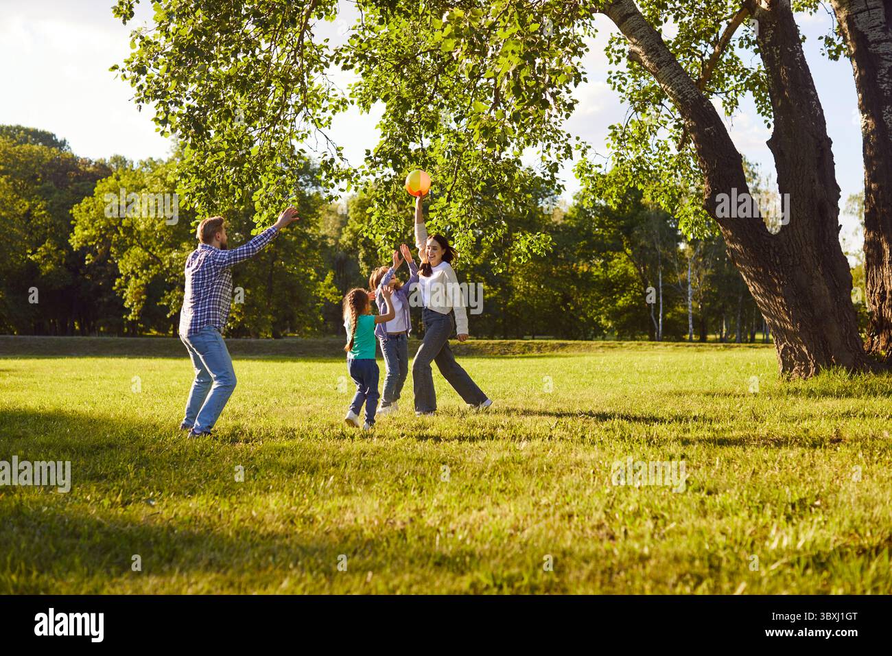 Happy smiling family playing together with a ball in the park at summer ...