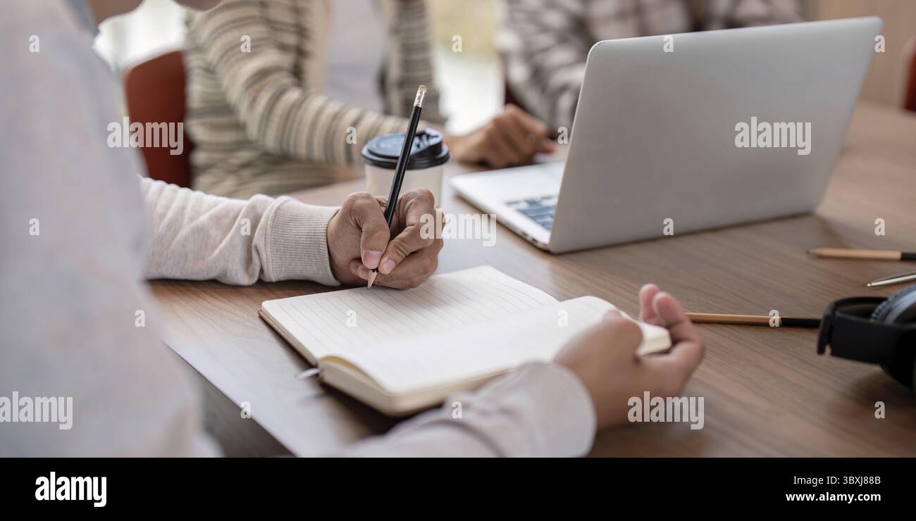 Students collaborating on a project, using laptops and notebooks, in a modern classroom environment Stock Photo