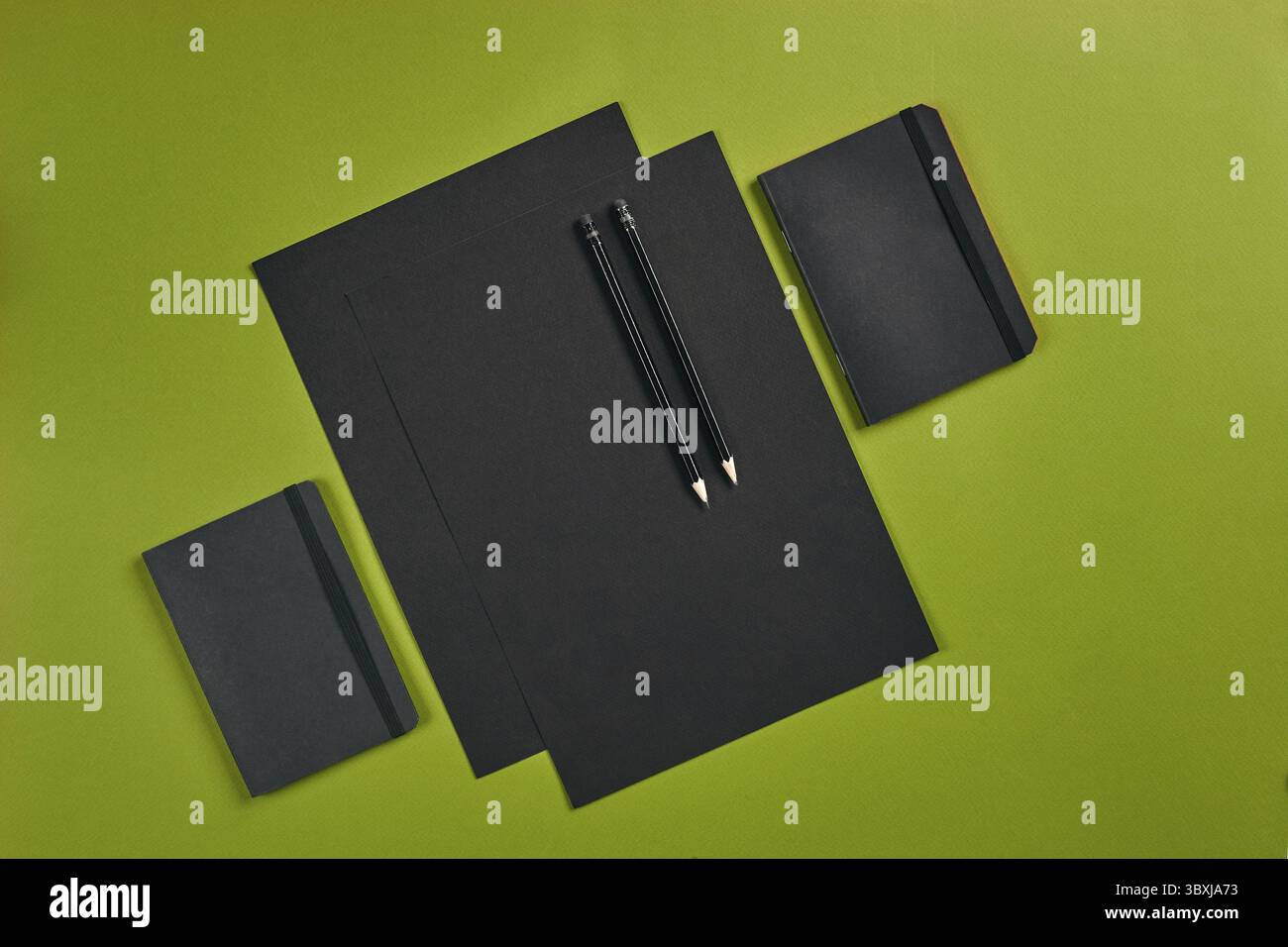 Two sheets of black paper, pencils and folders on green background with ...
