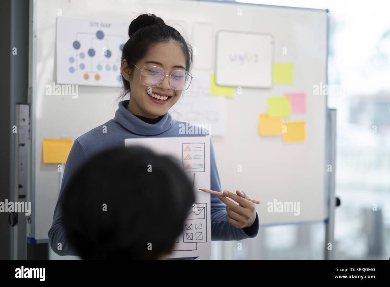 UX developer and UI designer collaborating on project ideas, using wireframes and flowcharts on a whiteboard in a modern office setting Stock Photo