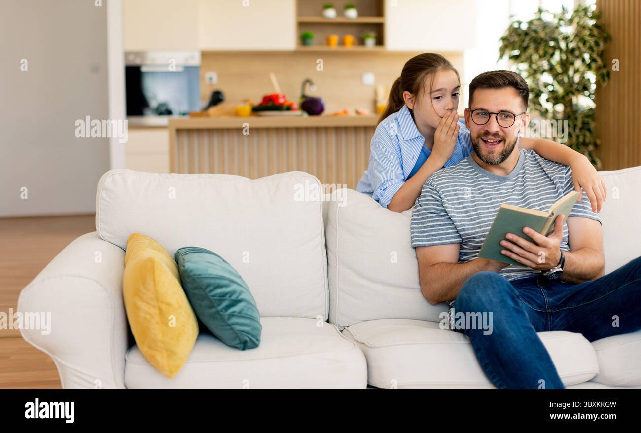A cheerful father shares a wonderful story with his daughter in their bright and inviting living room, filled with warm colors and cozy furniture that Stock Photo