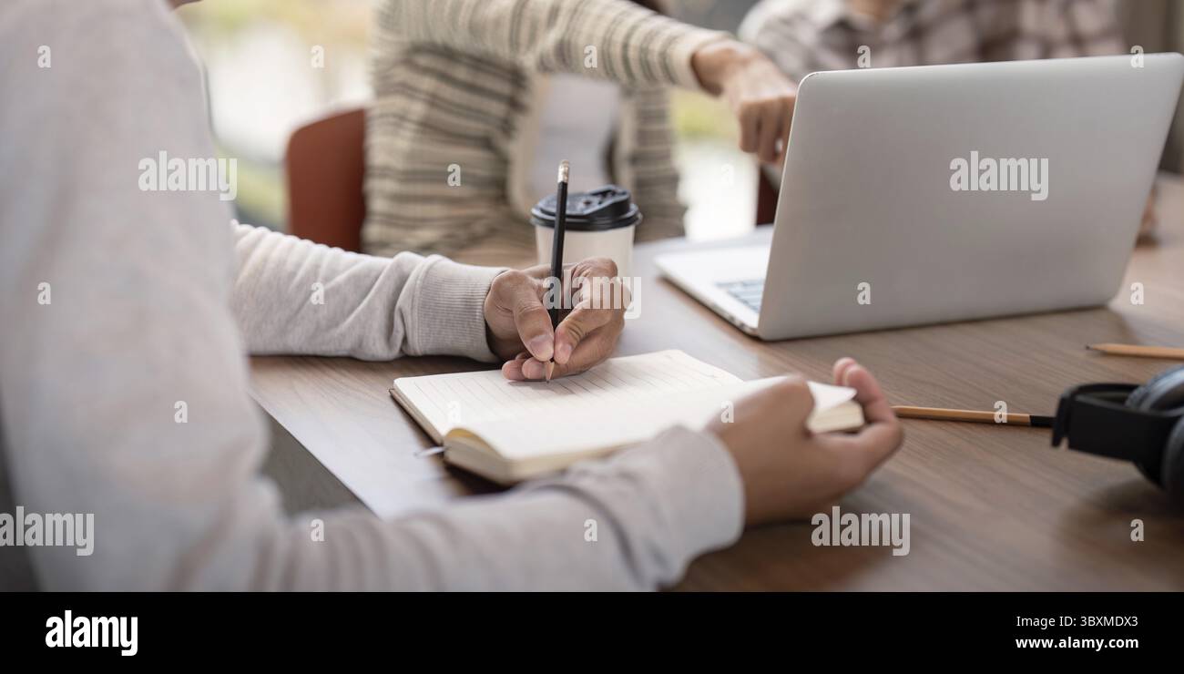 Students engaged in collaborative study session, using laptops and notebooks in a modern classroom environment Stock Photo