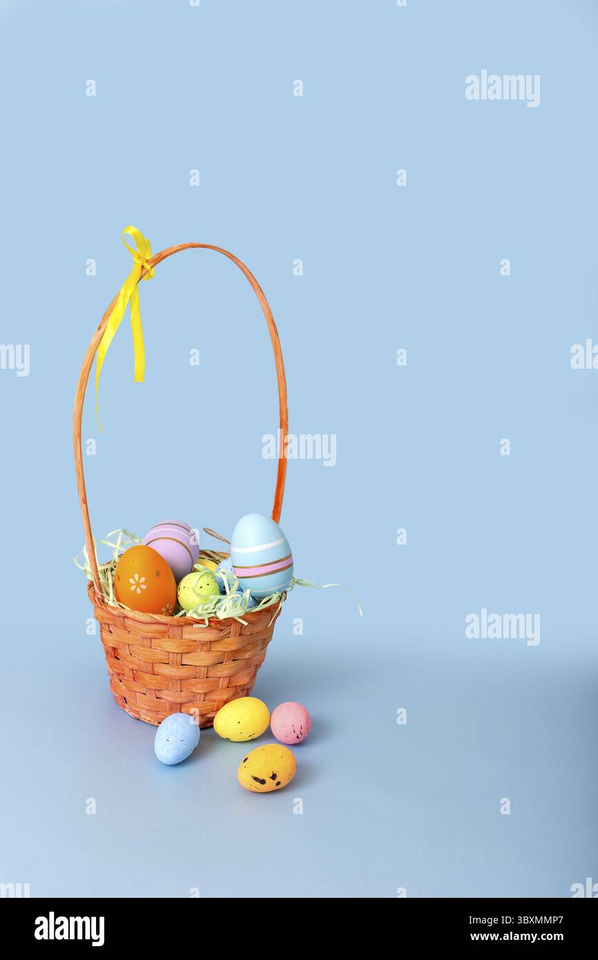 Easter basket filled with decorative multi colored eggs on a light blue background.Vertical Stock Photo