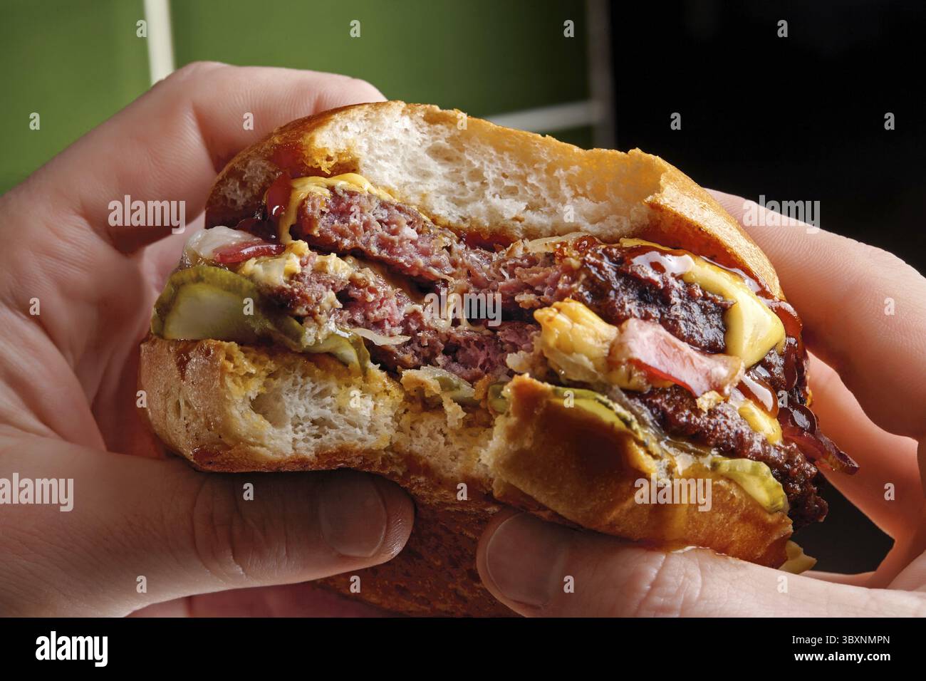 Two hands holding a bitten juicy double burger with melted cheese ...