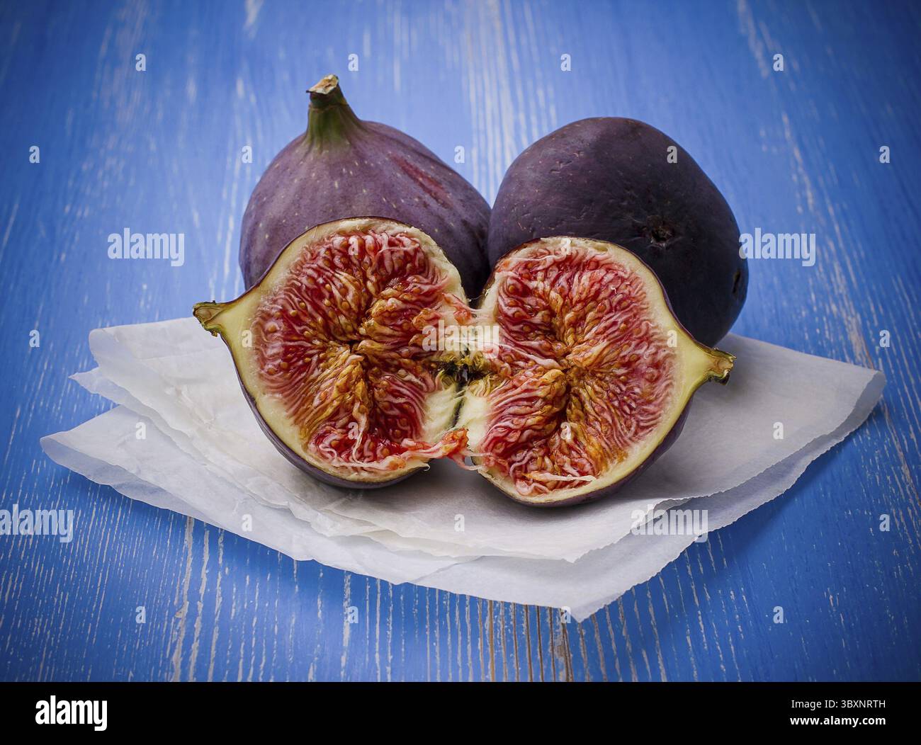 Three ripe figs on blue background, close up Stock Photo