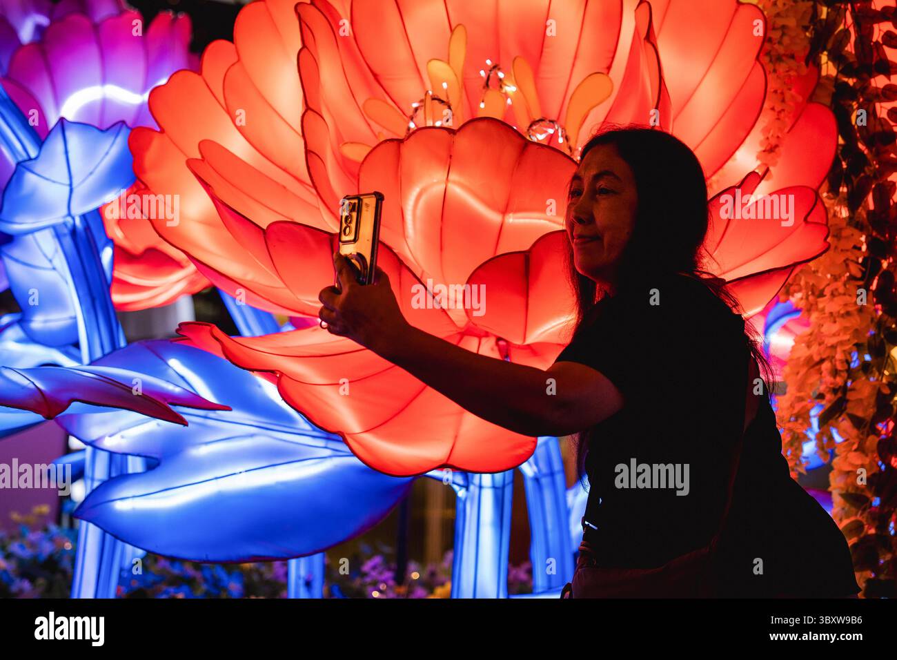 A woman takes a selfie in front of giant glowing flower lanterns at the ...