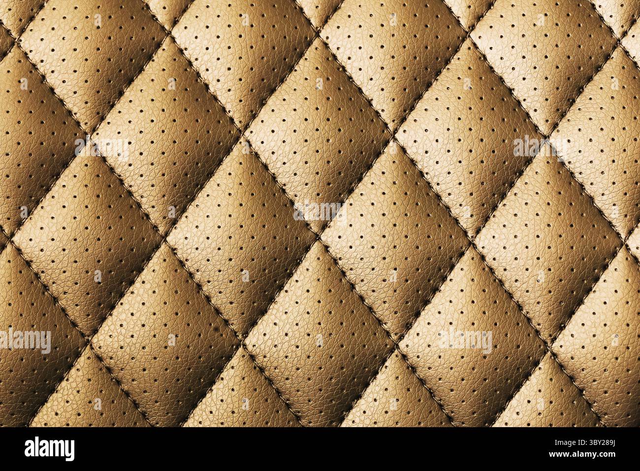Brown quilted leather texture with perforated surface. Diamond pattern close-up of stitched upholstery material. Soft padded leather background. Stock Photo