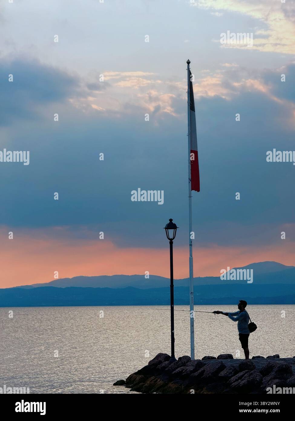 Man fishing from jetty at sunset at Cisano on Lake Garda Italy - Smartphone Captured Stock Image