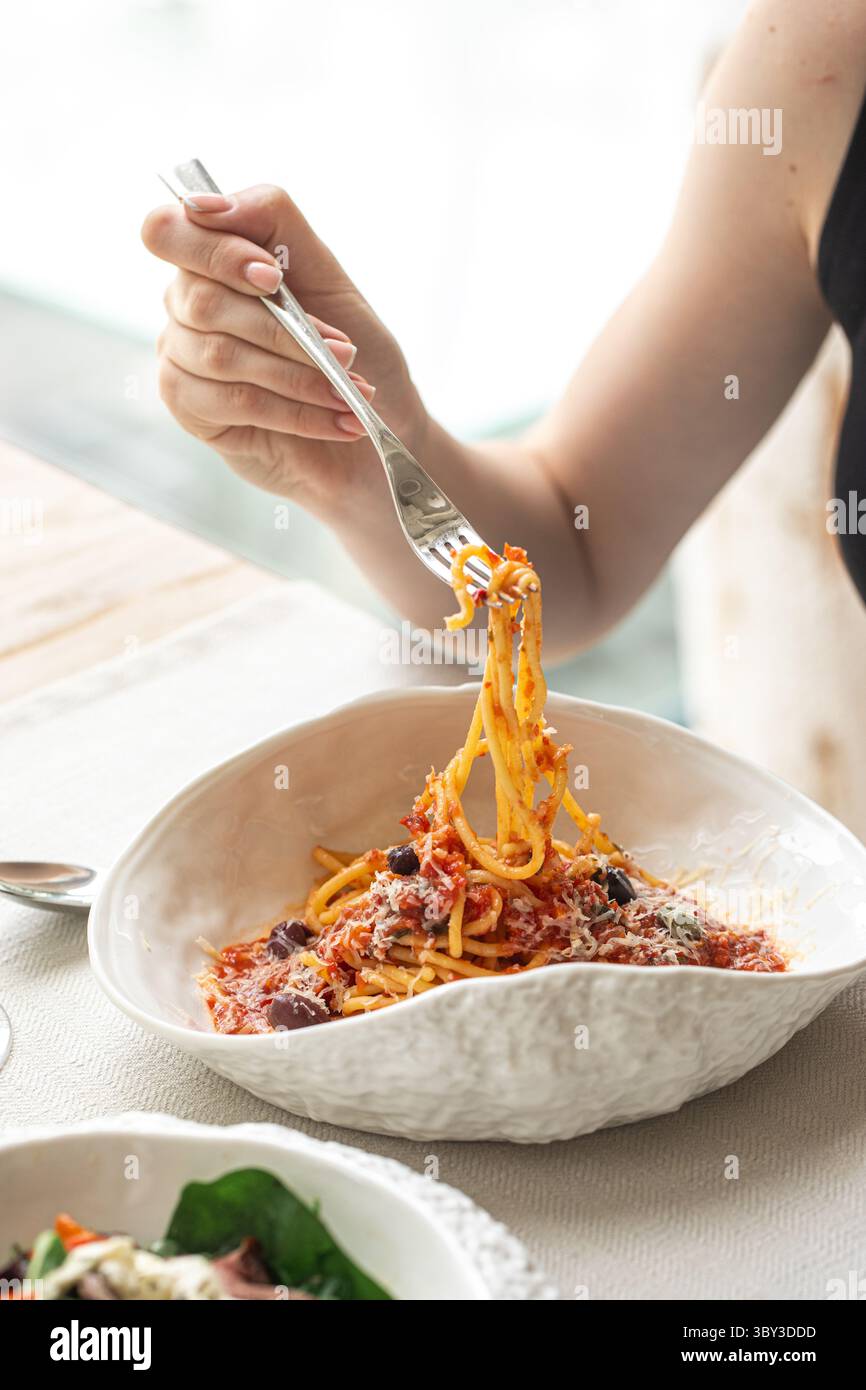 Woman twirling spaghetti with tomato and olives Stock Photo