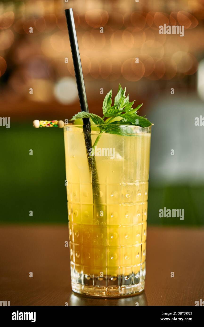A glass filled with a refreshing mango cocktail, garnished with mint leaves and served with a straw, sits invitingly on a wooden table against a warm Stock Photo
