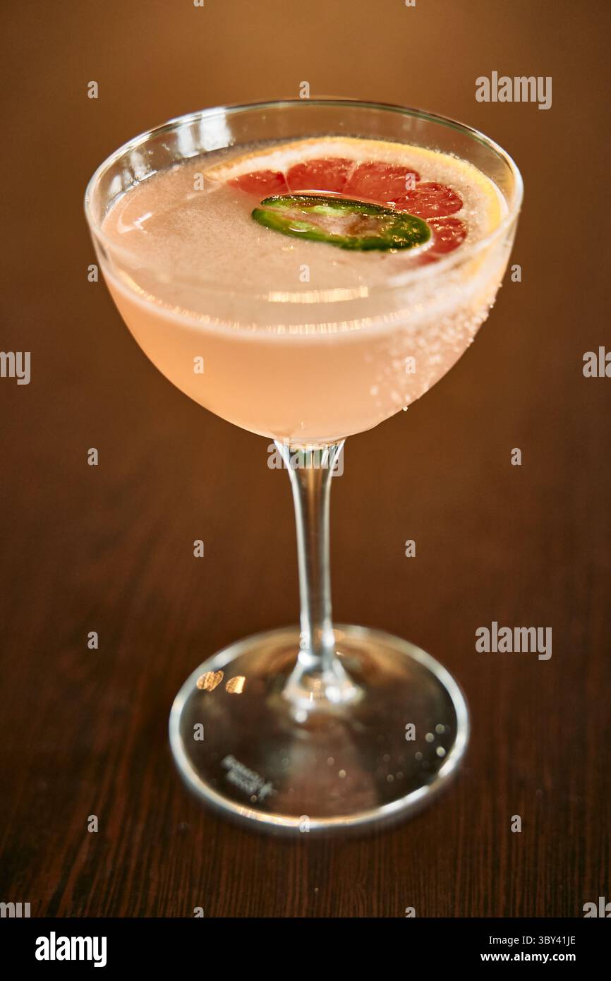 A sophisticated cocktail featuring grapefruit and jalapeño, elegantly served in a glass on a wooden table, offering a refreshing and spicy twist. Stock Photo