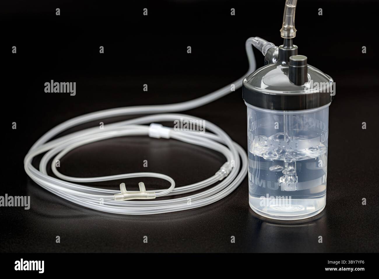 A medical oxygen humidifier bottle with attached tubing on black ...