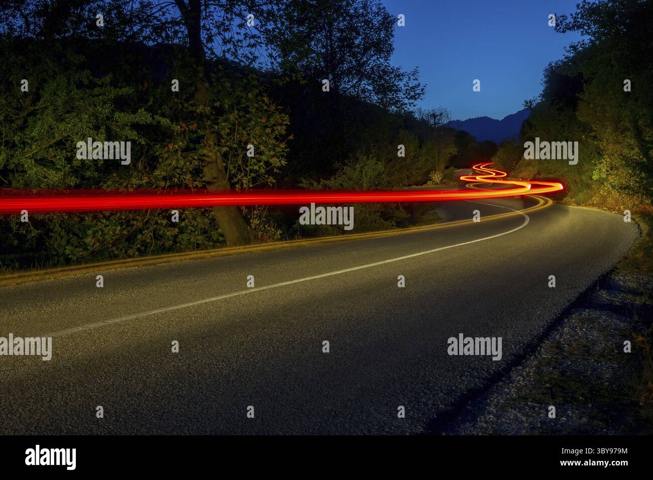 Taillights illuminate an empty road in a summer night forest. Long winding trails Stock Photo