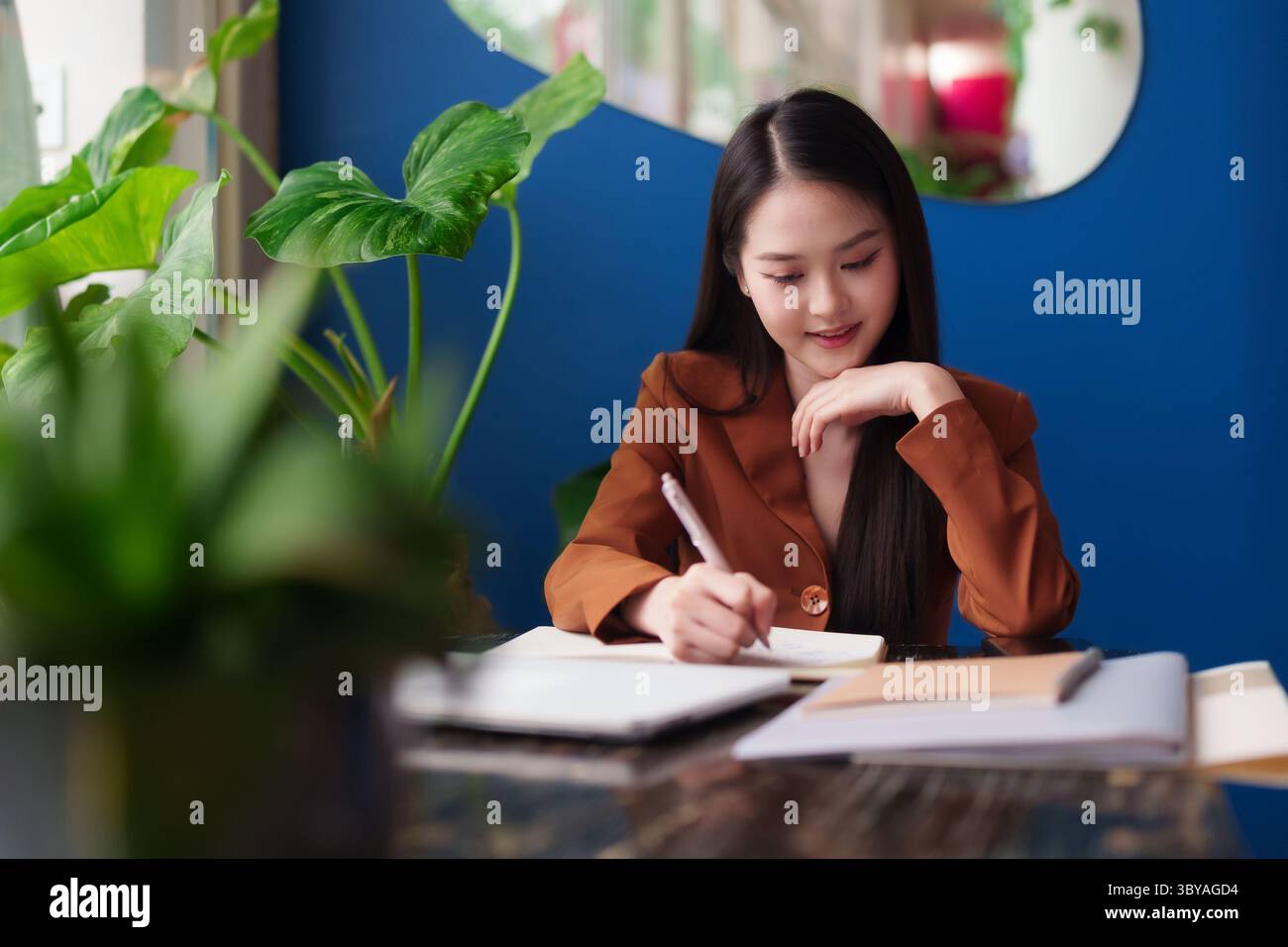 Prefessional Taking Notes Confident Asian professional diligently taking notes at her desk in a ...