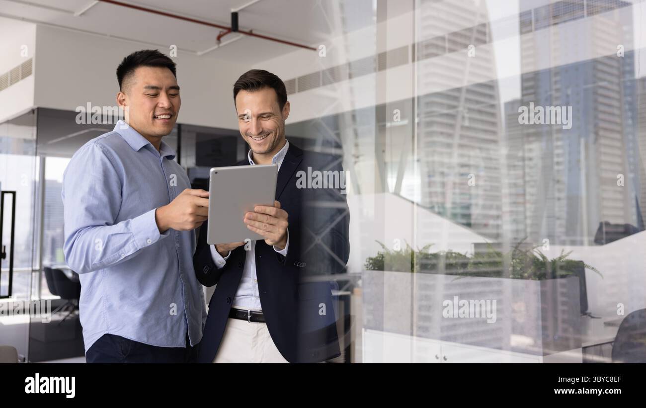 Two smiling men team members standing in office using tablet Stock Photo