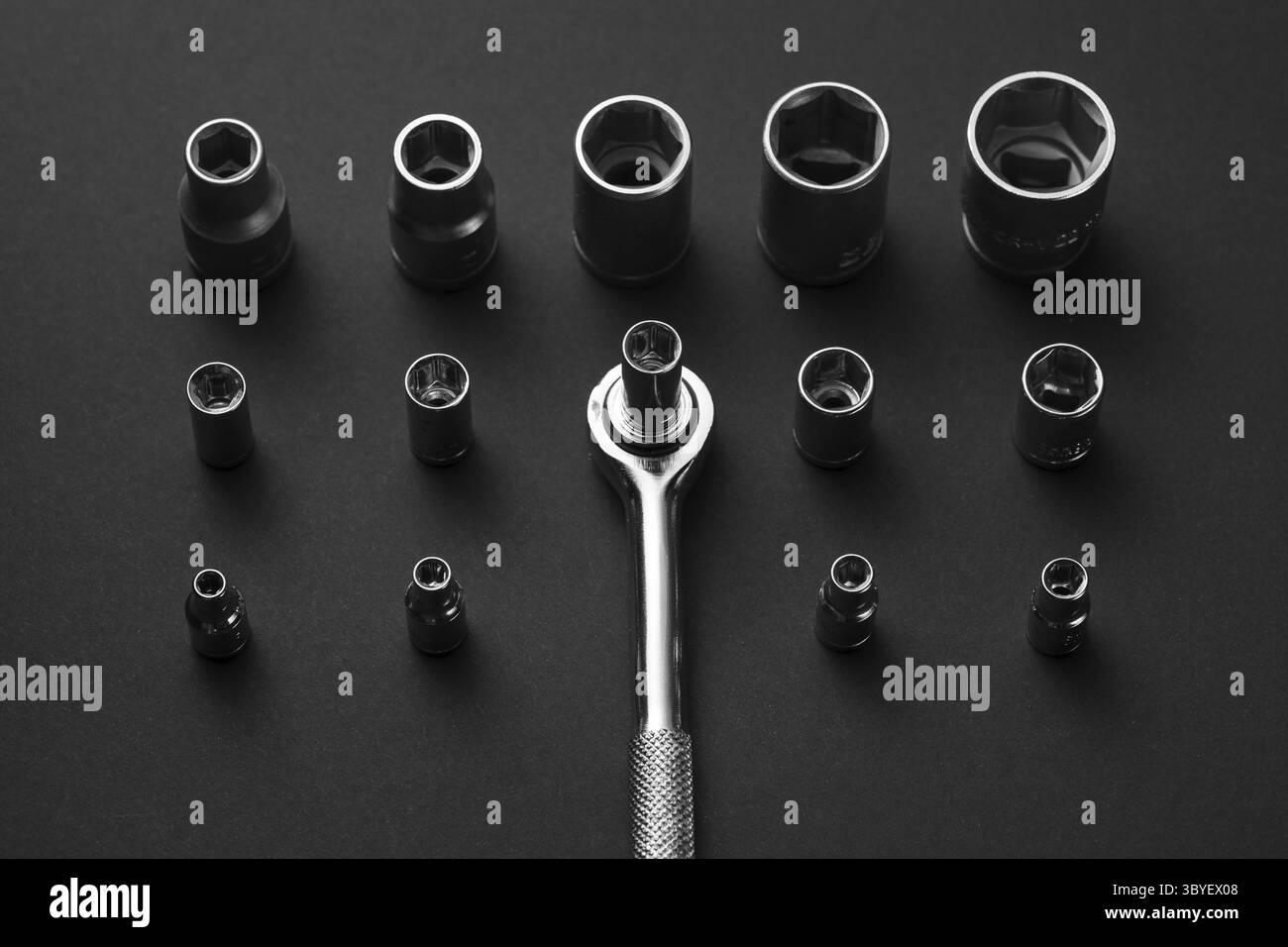 A collection of chrome socket wrenches and adapters are arranged on a dark gray surface. The wrenches vary in size and shape, with a single wrench Stock Photo