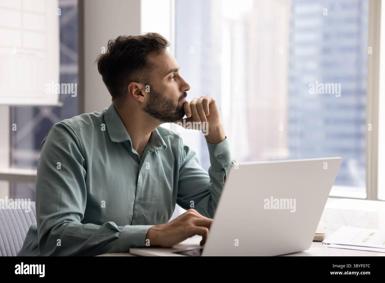 Pensive Latin man distracted from workflow looking out window Stock Photo