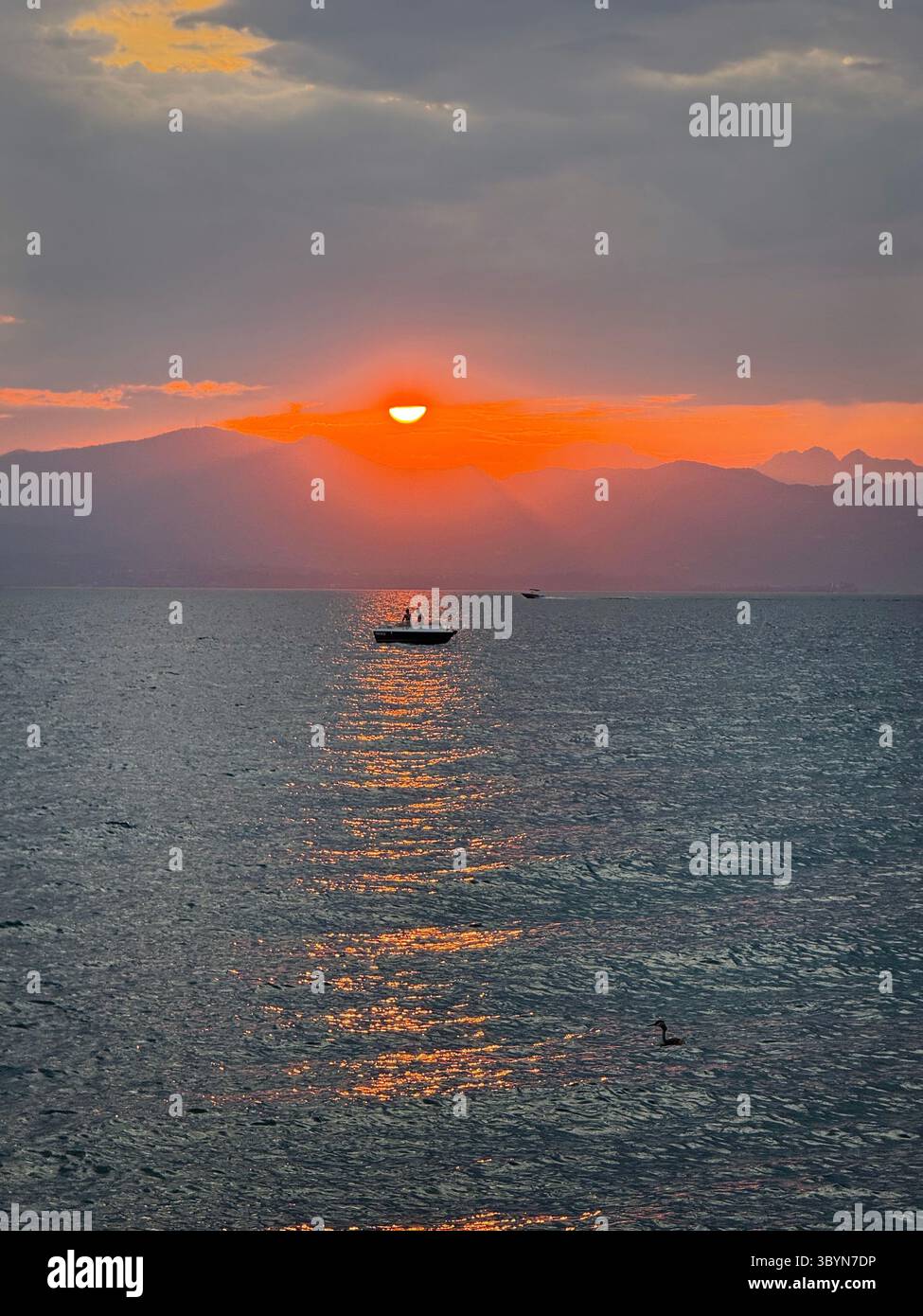 Sunset over Lake Garda from Cisano near Botdolino.  Boat in reflections from setting sun - Smartphone Captured Stock Image