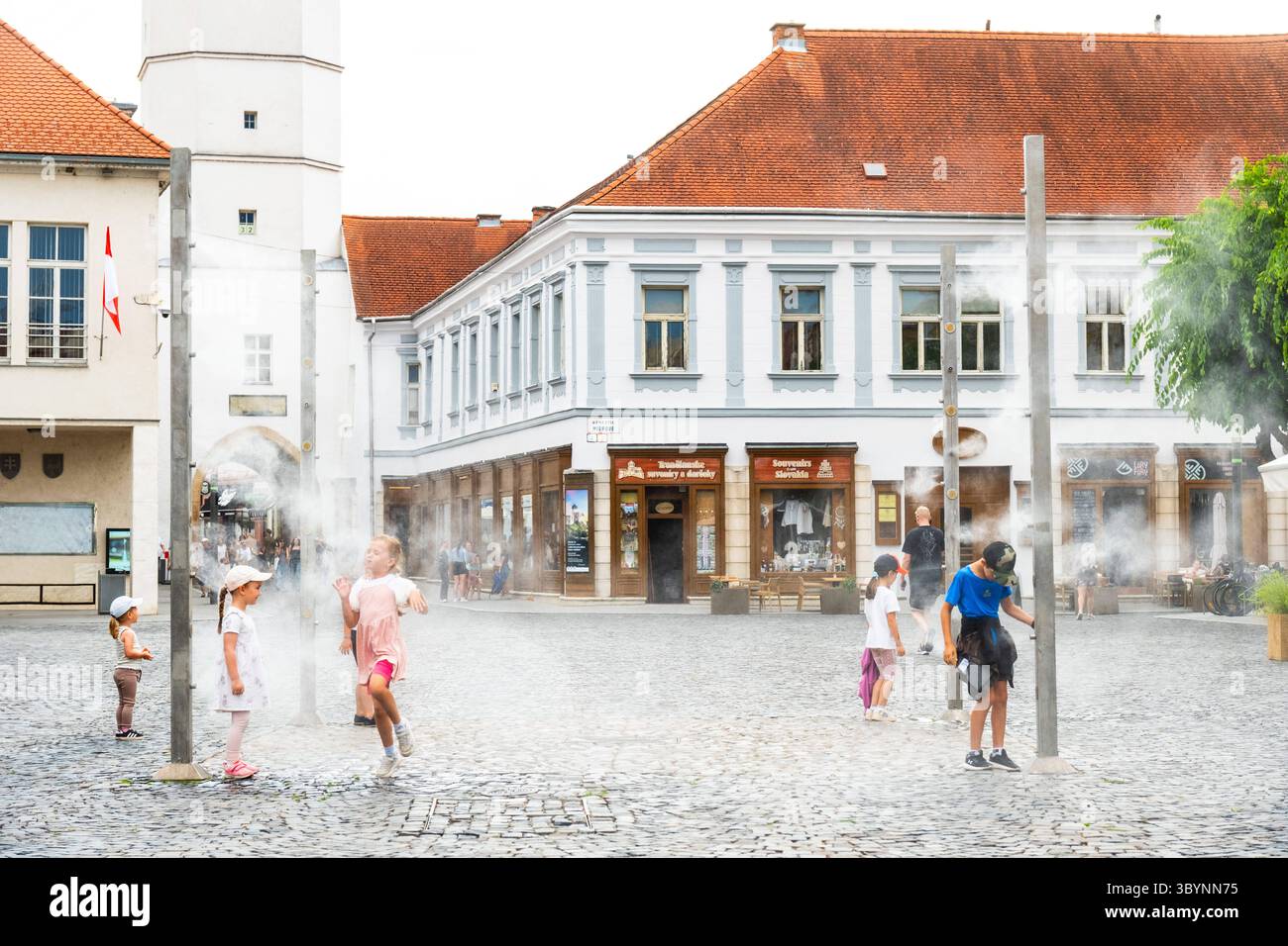Wassernebelanlage im Stadtzentrum von Trencin, Kinder nutzen die Erfrischung bei sommerlicher Hitze, TrenÄin, Slowakei editorial use only *** Water mi Stock Photo