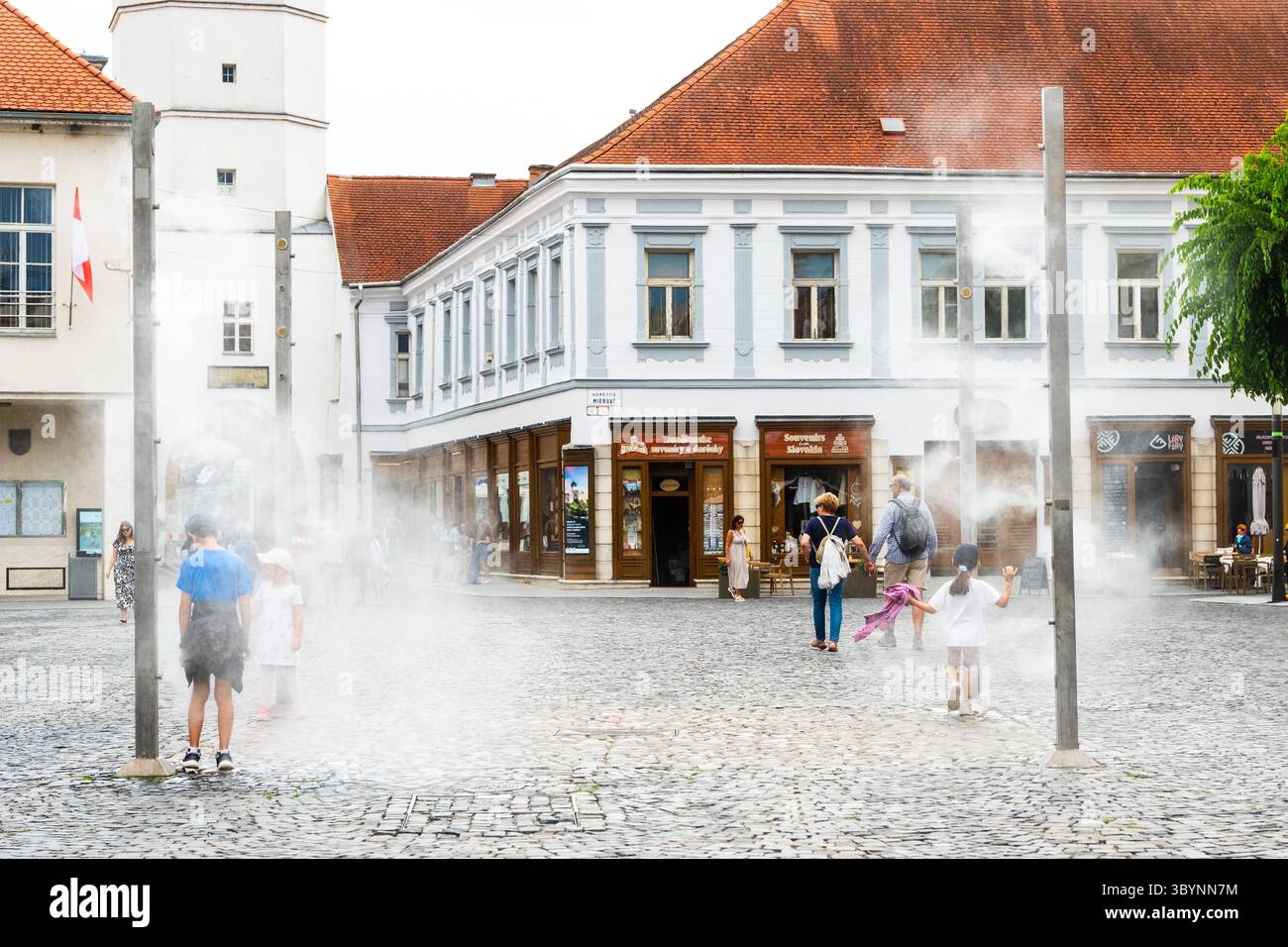 Wassernebelanlage im Stadtzentrum von Trencin, Kinder nutzen die Erfrischung bei sommerlicher Hitze, TrenÄin, Slowakei editorial use only *** Water mi Stock Photo