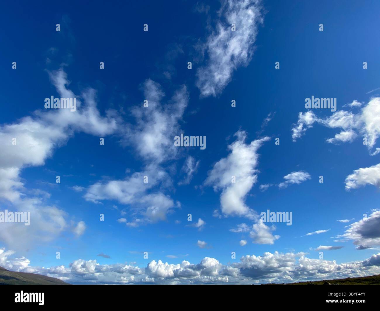 The vibrant blue sky is filled with puffy white clouds on a beautiful day. - Smartphone Captured Stock Image