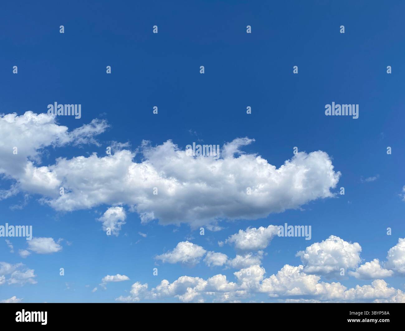 The vibrant blue sky is filled with puffy white clouds on a beautiful day. - Smartphone Captured Stock Image