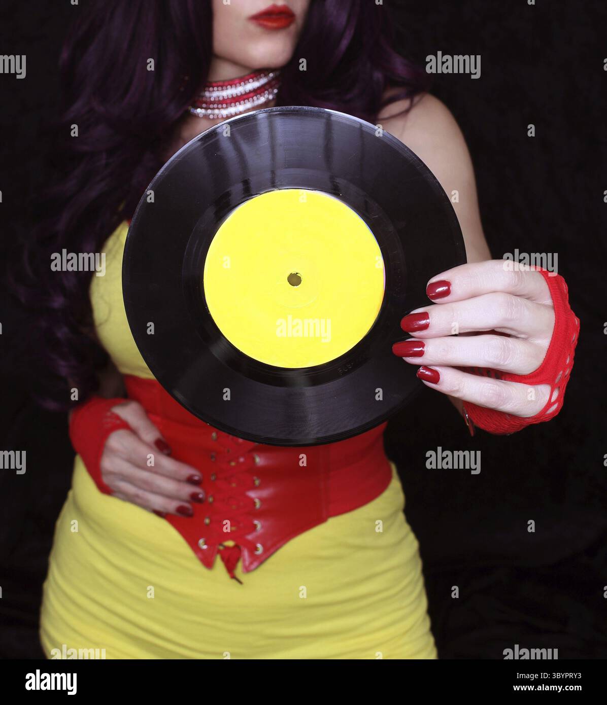 Frau in den 1980er Jahren gelbe Kleidung mit 45 rpm Rekord. Plattenlabel mit gelber Plakatfarbe lackiert Stock Photo