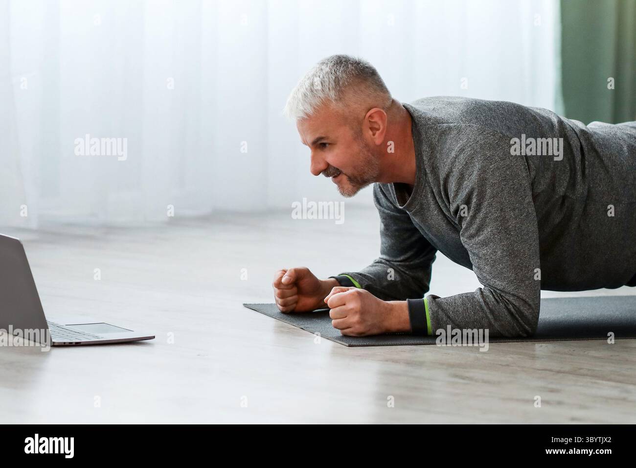 Athletic bearded older man doing exercises at home, using laptop Stock Photo