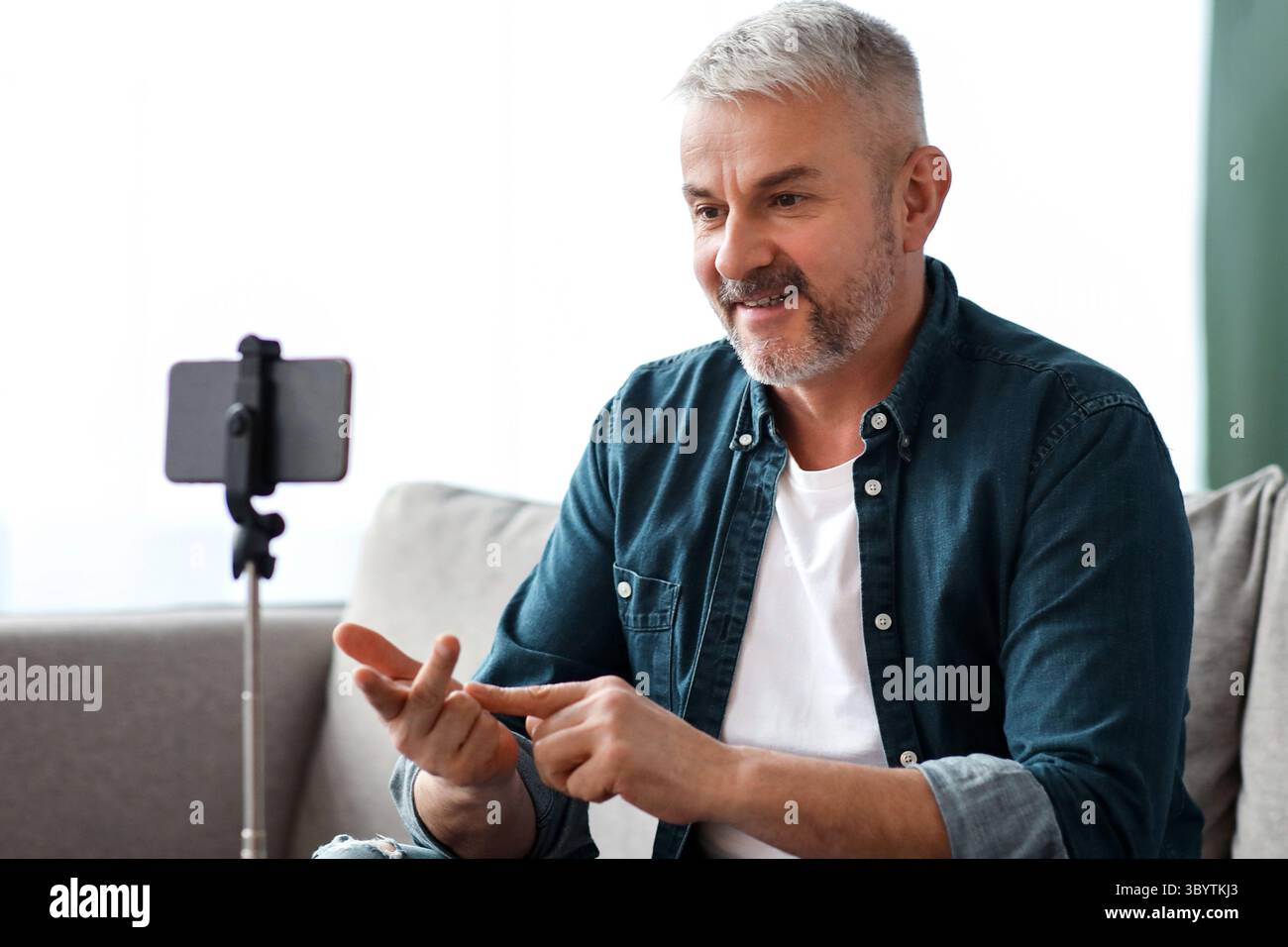 Cheerful matured man broadcasting from home, using smartphone Stock Photo