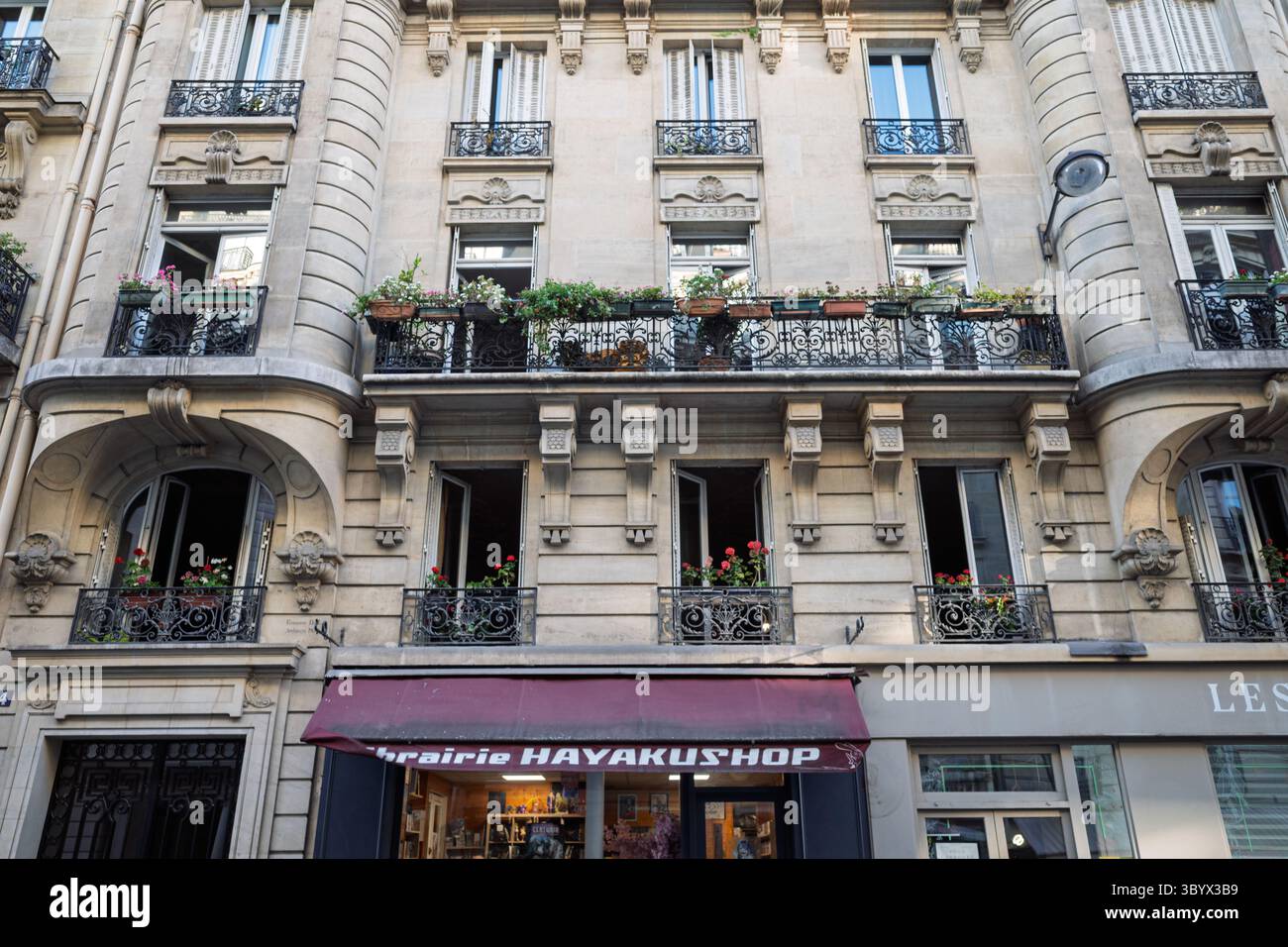 A beautiful old Parisian building facade with classic balconies adorned with blooming flowers and a charming bookstore below. Stock Photo